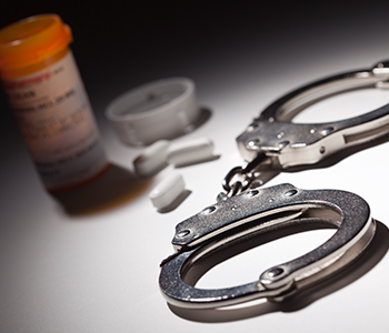 Handcuffs and various pills arranged on a wooden table